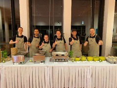 dean&david Catering | Stuttgart - Freundliches Catering Team hinter einer Buffetstation mit warmen Speisen, Saucen und frischen Kräutern für eine professionelle Eventbewirtung.