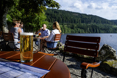 Der Biergarten des Maritim Hotels Titisee lädt mit gemütlichen Sitzplätzen im Freien und rustikalem Charme zum Entspannen ein. Gäste genießen erfrischende Getränke und Snacks in einer angenehmen Umgebung.