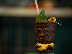 Exotischer Tiki-Cocktail im verzierten Becher mit Limette, Minze und Trinkhalm – stimmungsvoll angerichtet auf tropischem Blatt.