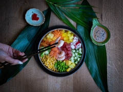 Bunte Poké Bowl mit Garnelen, Mais, Edamame, Mango und Karotten – liebevoll serviert auf tropischen Blättern mit Dips und Stäbchen.