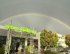 Sonnenlicht nach einem Regenschauer über dem Denns BioMarkt. Ein deutlich sichtbarer Regenbogen spannt über das Marktgebäude. Aufgenommen von einem zufriedenen Kunden.
