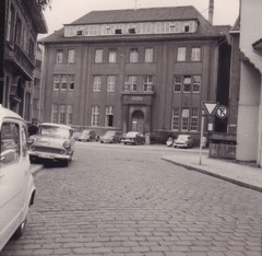 Eine historische Aufnahme des Rathauses II in Oldenburg mit Blick auf die gepflasterte Straße und parkende Autos aus vergangenen Jahrzehnten. Das Bild vermittelt den Charme des alten Stadtbildes.