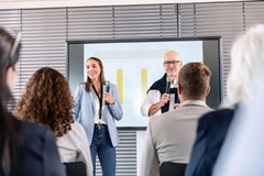 Ein professionell ausgestatteter Konferenzraum in der Alten Stadtkasse Oldenburg, der sich ideal für Schulungen, Vorträge und Präsentationen eignet. Auf dem Bild halten zwei Vortragende eine Präsentation vor einem aufmerksamen Publikum. Der Raum ist mit m