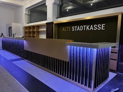 Der modern gestaltete Empfangsbereich der Alten Stadtkasse in Oldenburg beeindruckt mit einer stilvollen Kombination aus goldenen und dunklen Akzenten sowie einer beleuchteten Theke. Dieser einladende Raum ist der zentrale Punkt für Besucher, sei es für M