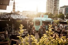 FirstLoveCoffee GmbH - Kaffee Catering Berlin - Mobiler Kaffeeanhänger bei Outdoor-Event in der Stadt mit Gästen, Musikbereich und Kaffeespezialitäten für Firmenfeier, Sommerfest oder Kundenveranstaltung.