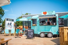 FirstLoveCoffee GmbH - Kaffee Catering Berlin - Mobiler Kaffeeanhänger mit Barista, Bio-Kaffee, frischen Waffeln und Sitzbereich bei sonnigem Outdoor-Event, passend für Sommerfest und Event Catering.