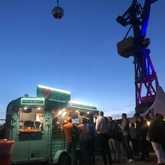 FirstLoveCoffee GmbH - Kaffee Catering Berlin - Beleuchteter Kaffeeanhänger am Abend bei Eventlocation mit Gästen, Barista-Service, Bio-Kaffee und mobilen Kaffeespezialitäten für Outdoor-Veranstaltungen.