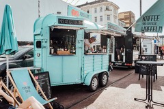 FirstLoveCoffee GmbH - Kaffee Catering Berlin - Mobile Kaffeebar mit Branding, Sonnenschirmen, Liegestühlen und Barista bei urbanem Event, ideal für Kaffee Catering mit frischen Waffeln.