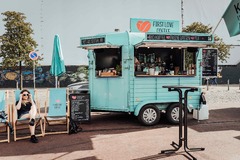FirstLoveCoffee GmbH - Kaffee Catering Berlin - Türkiser Kaffeeanhänger mit Bio-Kaffee, Tee, frischen Waffeln, Stehtischen und Barista-Service bei einer Outdoor-Veranstaltung in der Stadt.