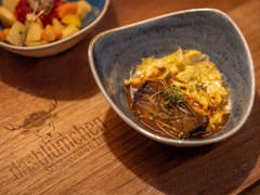 Tapasgericht mit Fleisch und Sauce auf Holzbrett mit Logo Das Blümchen Schwarzwald Tapas.