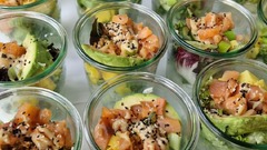 dean&david Catering | Pforzheim - Nahaufnahme von Lachs Bowls im Glas mit Avocado, Mango, Salat, Sesam und cremigem Dressing als frische Bowl-Auswahl für Events.