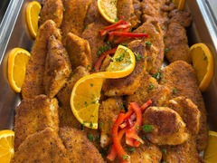 Die Feinschmecker Catering & Partyservice Hamburg - Goldbraun panierte Schnitzel und saftige Hähnchenstecks in einem Chafing Dish Behälter, garniert mit frischen Orangenscheiben und roten Paprikastreifen für das warme Buffet.