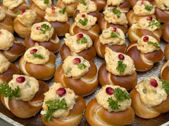 Die Feinschmecker Catering & Partyservice Hamburg - Herzhaftes Fingerfood aus Mini-Laugenknoten, garniert mit einer feinen Creme, frischer Petersilie und Granatapfelkernen, serviert auf einer edlen silbernen Servierplatte.