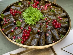 Die Feinschmecker Catering & Partyservice Hamburg - Traditionelle gefüllte Weinblätter (Dolmades) als vegane und vegetarische Vorspeise, kreisförmig auf einer Platte drapiert mit Salat, roten Johannisbeeren und Granatapfelkernen.