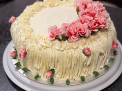 Die Feinschmecker Catering & Partyservice Hamburg - Festliche, weiße Cremetorte mit elegantem Wellenmuster, üppig dekoriert mit frischen rosa Nelken und Knospen als kulinarisches Highlight für Hochzeiten oder Jubiläen.