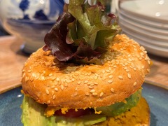 Die Feinschmecker Catering & Partyservice Hamburg - Herzhafter Sesam-Bagel aus der Nahaufnahme, reichlich belegt mit cremigem Hummus, reifer Avocado, Tomaten und knackigem Salatblatt als moderner Snack für Business-Meetings.
