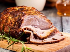 Die Feinschmecker Catering & Partyservice Hamburg - Zarter Krustenbraten, frisch aufgeschnitten auf einem Holzbrett mit Rosmarin. Warmes Fleischgericht als Highlight für das Hochzeitsbuffet oder Familienfeiern.