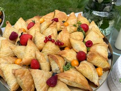 Die Feinschmecker Catering & Partyservice Hamburg - Goldbraun gebackene Teigtaschen auf einer dekorativen Buffetplatte mit Erdbeeren, Himbeeren und weiteren Beeren als herzhaftes Fingerfood für Veranstaltungen in Hamburg.