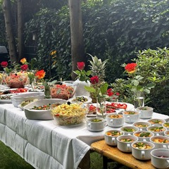 Die Feinschmecker Catering & Partyservice Hamburg - Reichhaltiges mediterranes Buffet bei einer Gartenparty im Grünen mit frischen Salaten, Antipasti, dekorativer Ananas, Rosen und kleinen Dessertschälchen im Vordergrund.
