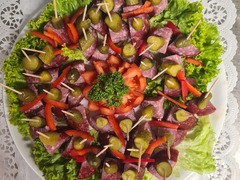 Die Feinschmecker Catering & Partyservice Hamburg - Liebevoll angerichtete kalte Platte aus der Vogelperspektive mit mundgerechten Salami-Häppchen auf Spießen, Gewürzgurken, Paprika und einer Tomatenrose im Zentrum.