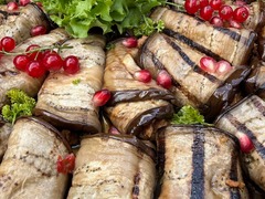 Die Feinschmecker Catering & Partyservice Hamburg - Gegrillte Auberginenröllchen auf einer großen Buffetplatte, dekoriert mit frischem Blattsalat, roten Johannisbeeren, Granatapfelkernen und Petersilie.
