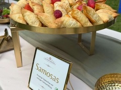 Die Feinschmecker Catering & Partyservice Hamburg - Goldbraun gebackene Samosas mit würziger Gemüsefüllung, dekorativ auf einer erhöhten Buffetplatte mit frischen Beeren angerichtet. Vegetarisches Fingerfood fürs Catering.