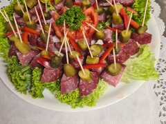Die Feinschmecker Catering & Partyservice Hamburg - Schön präsentierte Aufschnittplatte mit dekorativen Salami-Spießen, Gurkenstücken und frischem Blattsalat, perfekt geeignet als Snack für Stehempfänge und Meetings.
