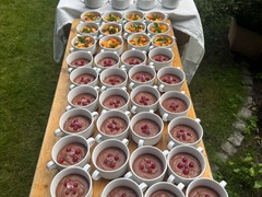 Die Feinschmecker Catering & Partyservice Hamburg - Lange Tafel im Freien mit einer großen Auswahl an süßen Nachspeisen, bestehend aus cremigem Schokoladenmousse mit Beeren und frischem, buntem Obstsalat in weißen Tassen.
